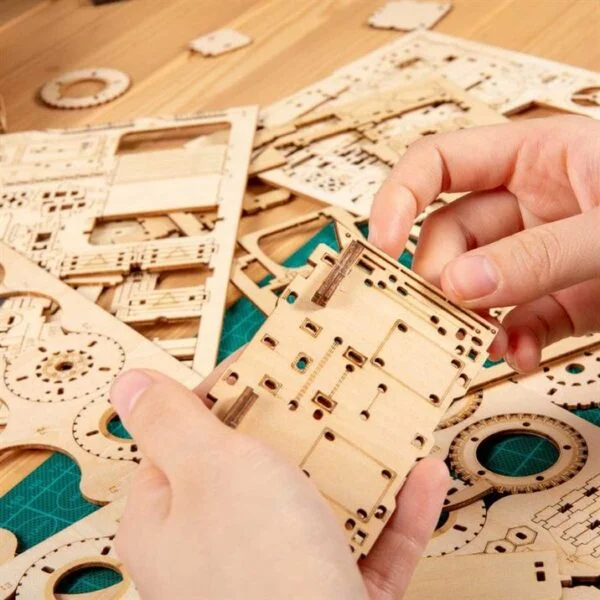 Une personne assemble une maquette en bois ROKR d'une horloge.