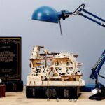 Une maquette de puzzle ROKR 3D présentant un modèle en bois d'une horloge et d'une lampe sur un bureau.