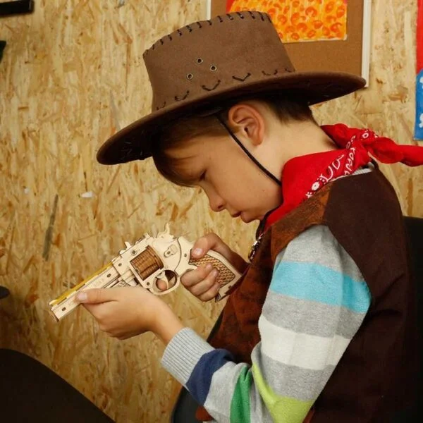 Un garçon portant un chapeau de cowboy assemblant un puzzle de pistolet en bois 3D de Robotime.