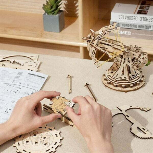 Une personne assemble un modÃ¨le de puzzle en bois 3d reprÃ©sentant une horloge de la sÃ©rie rokr de robotime.
