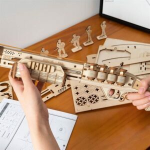 Une personne assemble un modèle en bois 3D d'une arme à feu à partir du puzzle Robotime.