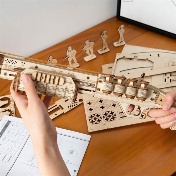 Une personne assemble un modÃ¨le en bois 3d d'une arme Ã  feu Ã  partir du puzzle robotime.
