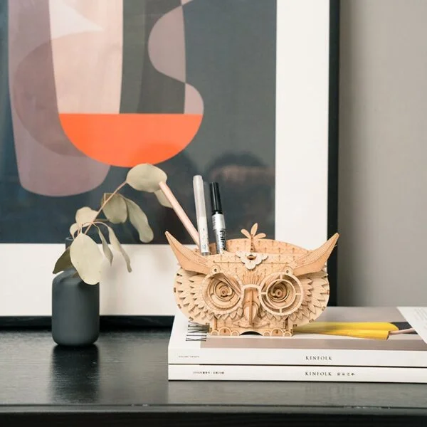 Un hibou en bois assis sur un bureau à côté d’un livre.