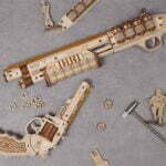 Un robotime Pistolet à élastique Corsac M60 + 100 élastiques et d'autres objets de type puzzfever sont disposés sur une table.