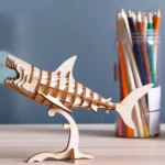 Un modèle de requin Puzzle ROKR en bois 3D de Robotime affiché sur une table avec des crayons.