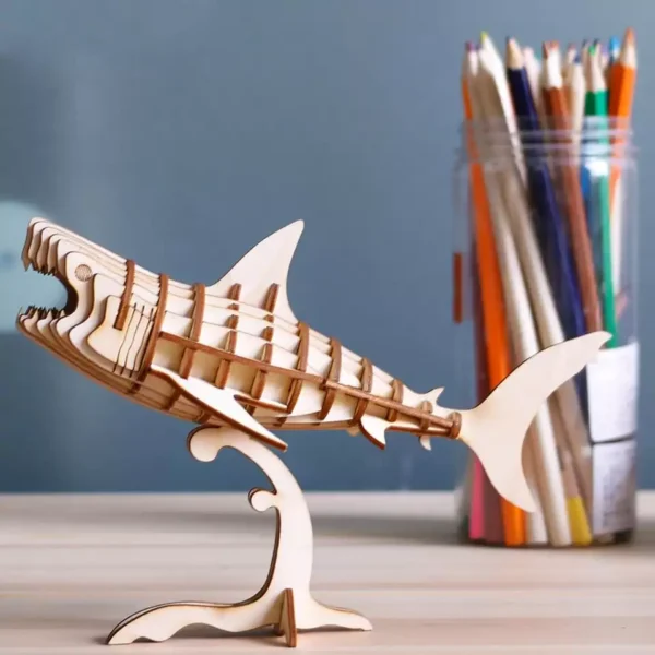Un modÃ¨le de requin puzzle rokr en bois 3d de robotime affichÃ© sur une table avec des crayons.
