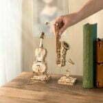 Une personne tenant un ROKR - Cello : maquette en bois violoncelle et un livre sur une table.
